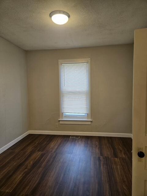 unfurnished room featuring dark wood-style flooring, baseboards, and a textured ceiling