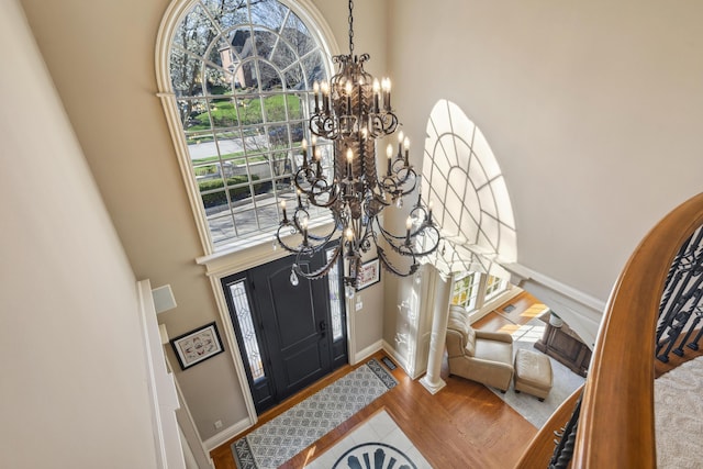 entryway with wood finished floors, a towering ceiling, baseboards, and a notable chandelier