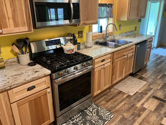 kitchen featuring stainless steel appliances, visible vents, a sink, dark wood-type flooring, and light stone countertops