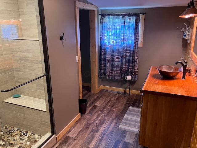 bathroom with baseboards, wood finished floors, a stall shower, and a sink