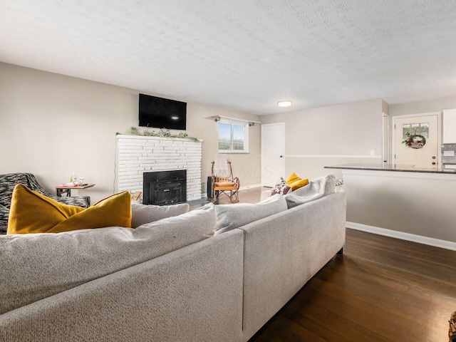 living room featuring a brick fireplace, a textured ceiling, baseboards, and wood finished floors