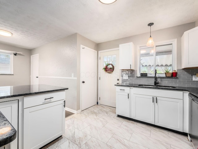 kitchen with dark stone counters, stainless steel dishwasher, white cabinets, a sink, and backsplash