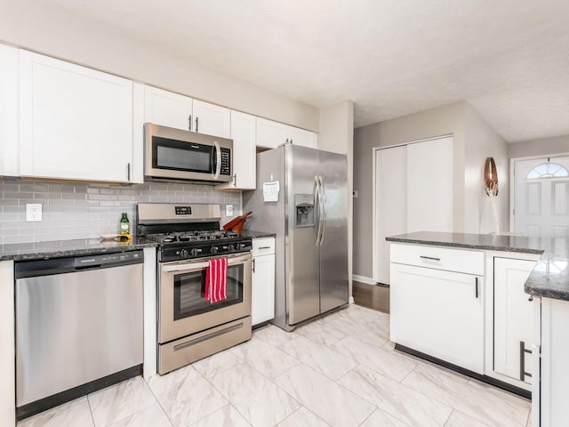 kitchen featuring dark stone countertops, decorative backsplash, white cabinets, and stainless steel appliances