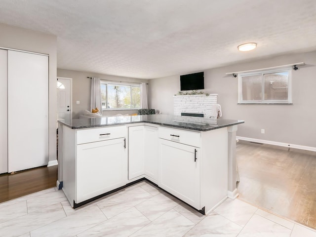 kitchen with dark stone countertops, white cabinetry, marble finish floor, and a fireplace