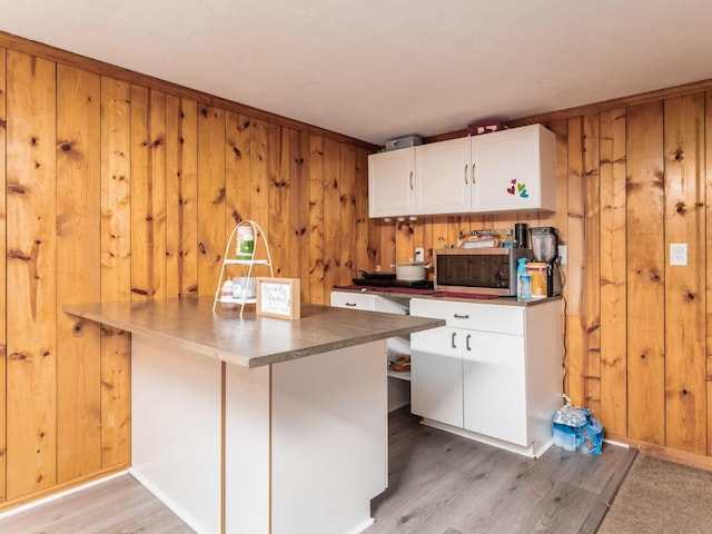 kitchen featuring white cabinets, light wood-type flooring, a breakfast bar, stainless steel microwave, and wood walls