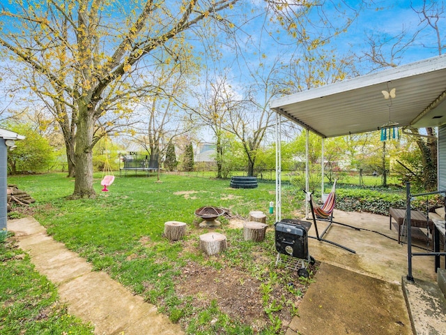 view of yard featuring a trampoline, a patio area, fence, and a fire pit