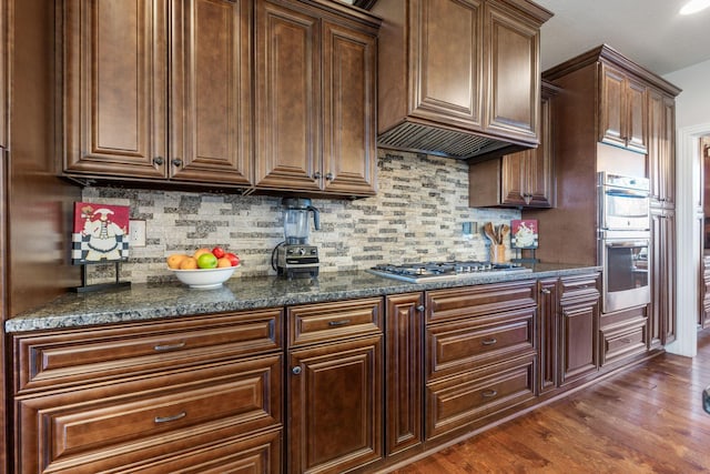 kitchen with appliances with stainless steel finishes, dark wood-style flooring, extractor fan, and backsplash