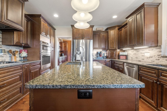 kitchen with decorative backsplash, appliances with stainless steel finishes, a kitchen island with sink, and dark stone counters