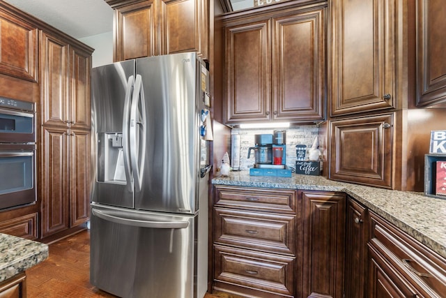 kitchen with stainless steel fridge with ice dispenser, multiple ovens, backsplash, and light stone counters