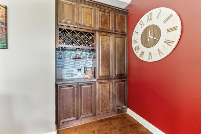 bar featuring a bar, backsplash, baseboards, and dark wood finished floors