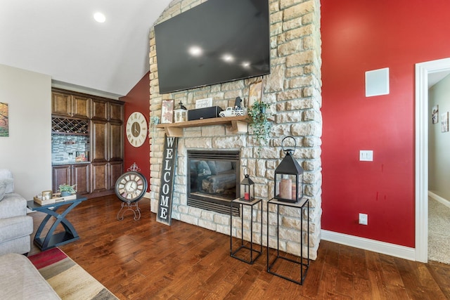 living room featuring wood finished floors, baseboards, a stone fireplace, and lofted ceiling
