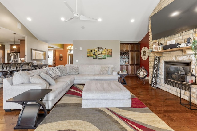 living room with a stone fireplace, high vaulted ceiling, wood finished floors, and ceiling fan with notable chandelier