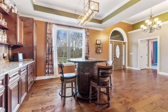 dining space with dark wood-style flooring, baseboards, ornamental molding, a chandelier, and a tray ceiling