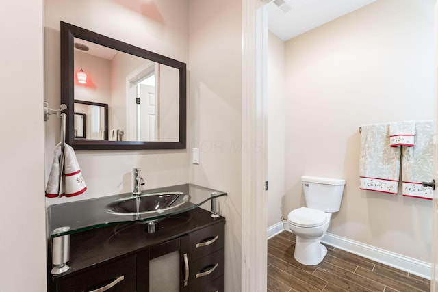 half bath with wood finish floors, vanity, visible vents, toilet, and baseboards