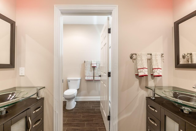 bathroom with toilet, wood finish floors, baseboards, and vanity