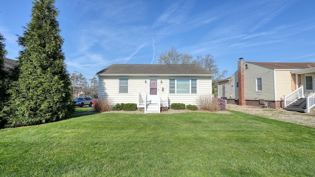view of front of property featuring entry steps, a front lawn, and a shingled roof