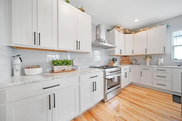 kitchen featuring wall chimney exhaust hood, high end stove, backsplash, and light wood-type flooring