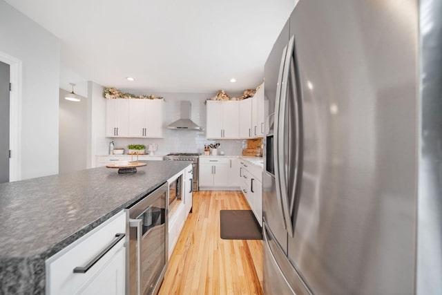 kitchen with wall chimney exhaust hood, stainless steel appliances, wine cooler, light wood-style flooring, and backsplash