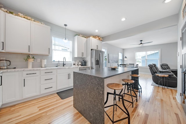 kitchen featuring light wood-style flooring, a sink, open floor plan, a kitchen bar, and stainless steel fridge with ice dispenser