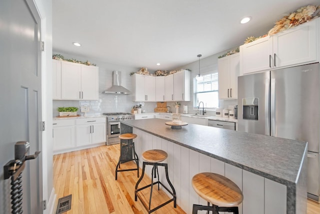 kitchen featuring wall chimney range hood, a sink, light wood-style floors, appliances with stainless steel finishes, and visible vents