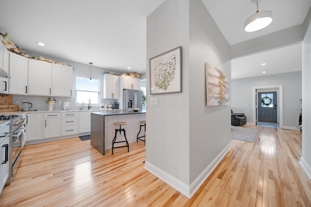 kitchen with light wood-type flooring, a kitchen breakfast bar, white cabinetry, and appliances with stainless steel finishes
