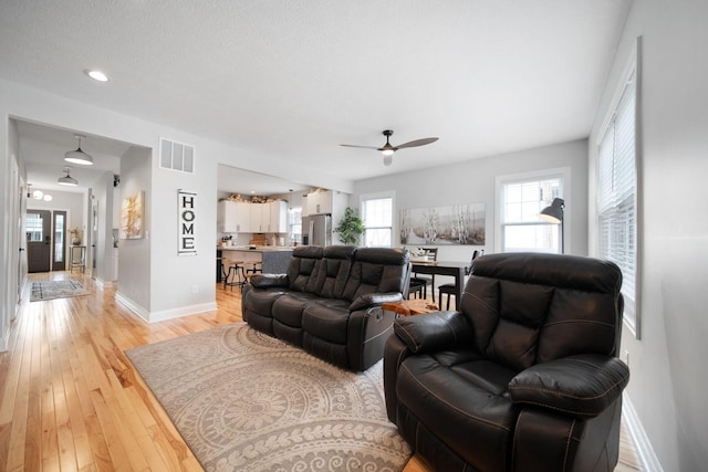 living room with baseboards, a ceiling fan, visible vents, and light wood-style flooring