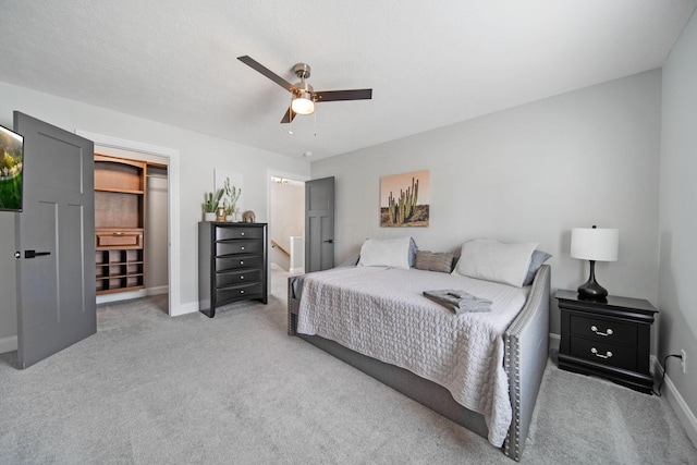 bedroom with a walk in closet, ceiling fan, baseboards, and carpet