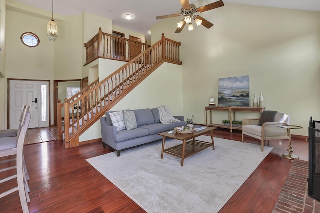 living room with baseboards, a high ceiling, wood finished floors, ceiling fan with notable chandelier, and stairs