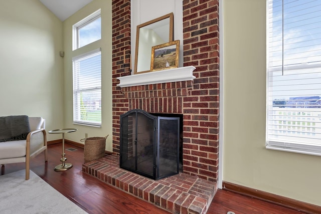 living area with a brick fireplace, baseboards, visible vents, and wood finished floors