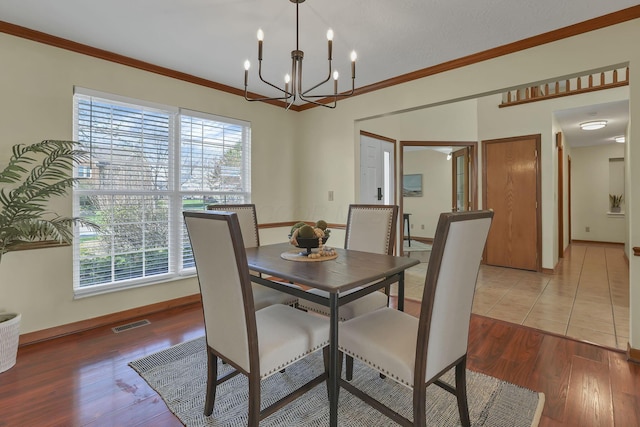 dining room featuring crown molding, light wood finished floors, a notable chandelier, and visible vents