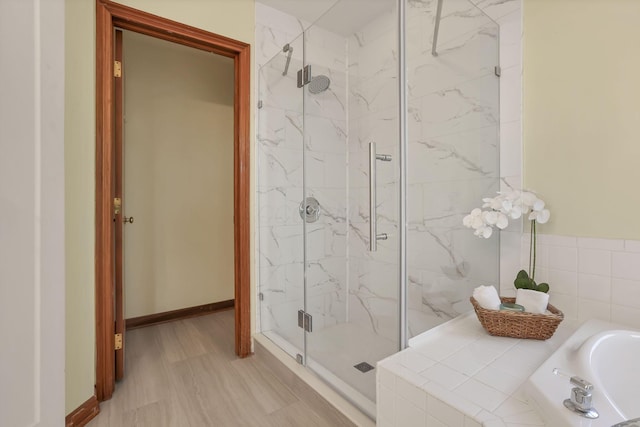 full bathroom featuring a garden tub, a marble finish shower, and baseboards
