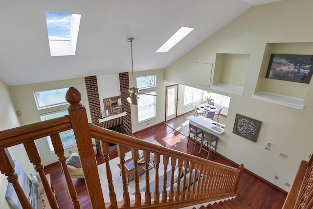 staircase featuring a skylight, wood finished floors, high vaulted ceiling, and a fireplace