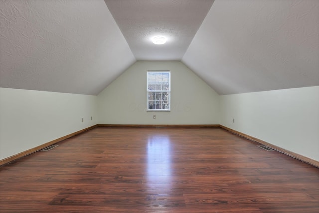 additional living space with a textured ceiling, wood finished floors, lofted ceiling, and visible vents