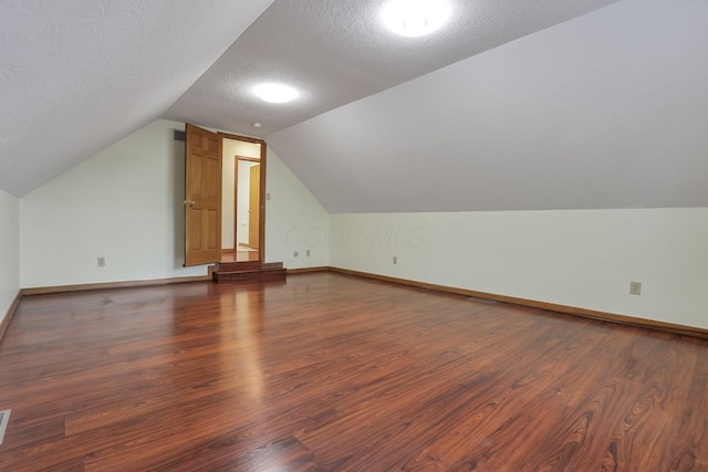 additional living space featuring baseboards, a textured ceiling, vaulted ceiling, and wood finished floors