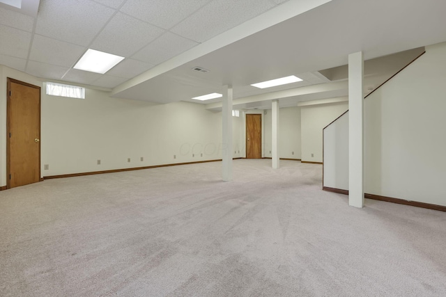 below grade area with visible vents, baseboards, a drop ceiling, and light colored carpet