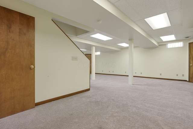 basement featuring a drop ceiling, baseboards, and carpet floors