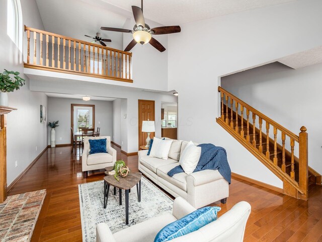 living room featuring wood finished floors, a towering ceiling, a ceiling fan, and stairway