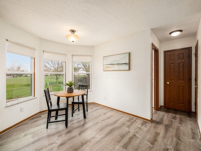 dining room with baseboards, light wood-type flooring, and a textured ceiling