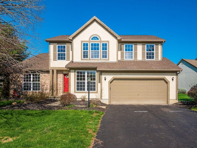 traditional-style house with aphalt driveway, stucco siding, roof with shingles, a front yard, and an attached garage
