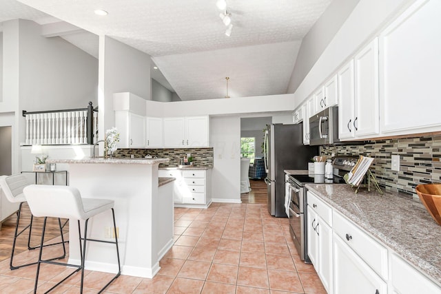 1148 Challis Springs Dr, New Albany, OH 43054 - kitchen with stainless steel appliances, light tile patterned floors, backsplash, white cabinetry, and vaulted ceiling