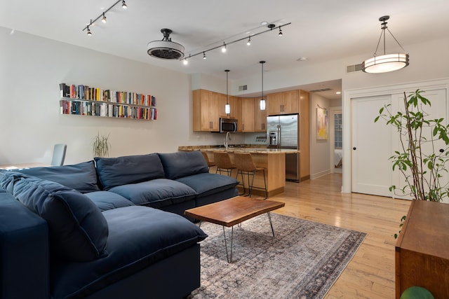 living room featuring track lighting, baseboards, light wood-style flooring, and visible vents