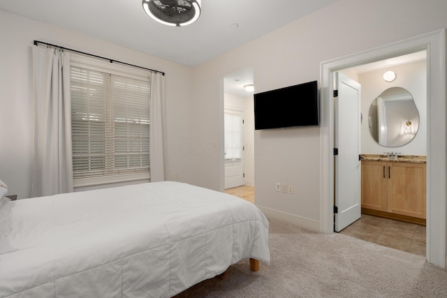 bedroom featuring baseboards, light colored carpet, a sink, and ensuite bath