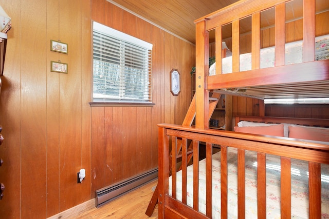 bedroom with wood walls, a baseboard radiator, and wood finished floors