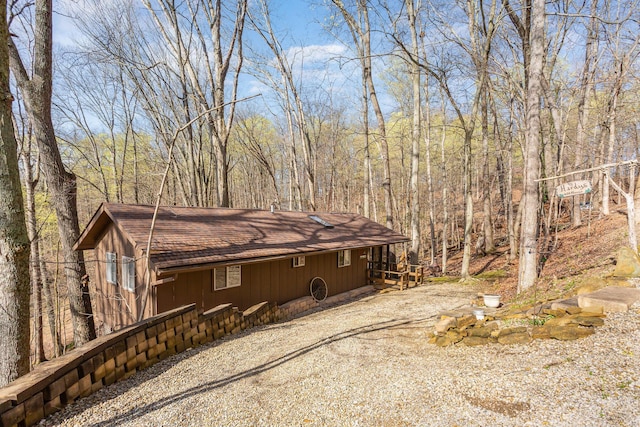 view of side of property with a wooded view and a shingled roof
