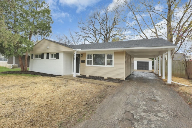 single story home featuring a carport, aphalt driveway, an outbuilding, fence, and a shingled roof