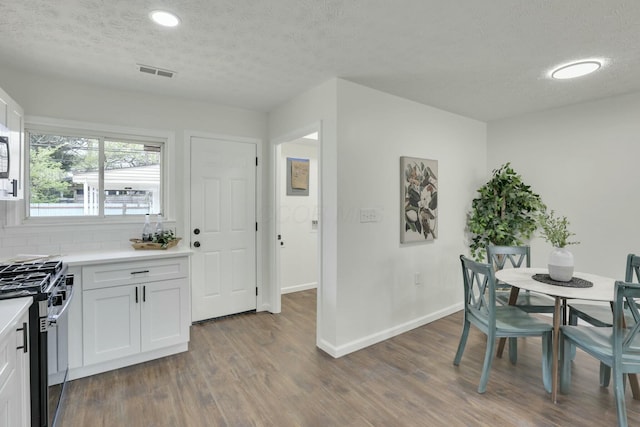 dining room featuring a textured ceiling, baseboards, dark wood finished floors, and visible vents