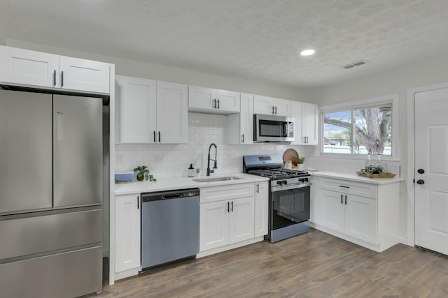 kitchen with tasteful backsplash, light countertops, a textured ceiling, stainless steel appliances, and a sink
