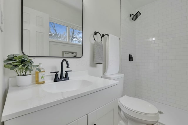 bathroom with tiled shower, vanity, and toilet