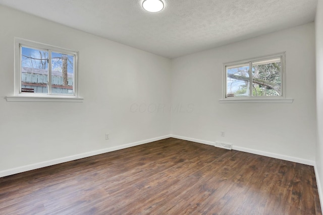 spare room with dark wood-type flooring, a textured ceiling, baseboards, and visible vents