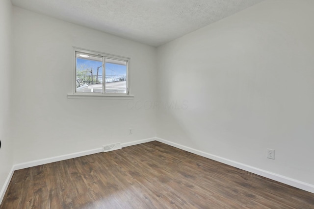 spare room with a textured ceiling, dark wood-style flooring, baseboards, and visible vents